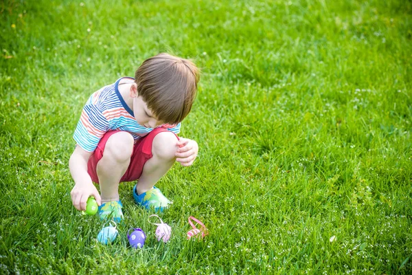 Mały chłopiec poluje na pisanki w wiosennym ogrodzie w Wielkanoc — Zdjęcie stockowe