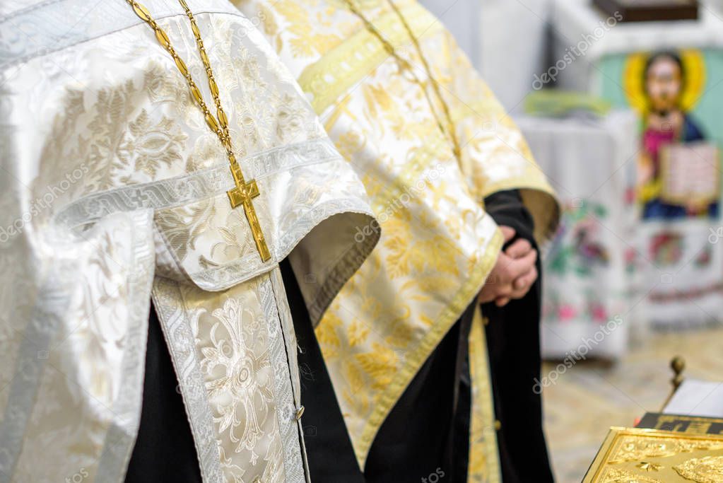Beautiful golden cross in male hands of priest wearing gold robe on ceremony in christian cathedral church, holy sacramental event. Priest Holding A Bible.
