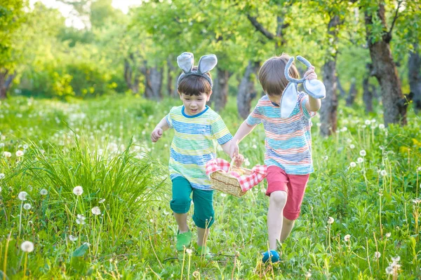 Kids on Easter egg hunt in blooming spring garden. Children searching for colorful eggs in flower meadow. Toddler boy and his brother friend kid boy play outdoors