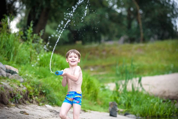 Retrato de niño caucásico en sombrero de paja jugando juguetes y bomba de agua en la playa . — Foto de Stock