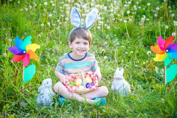 Malý chlapec loví velikonoční vejce v jarní zahradě o velikonočním dni — Stock fotografie