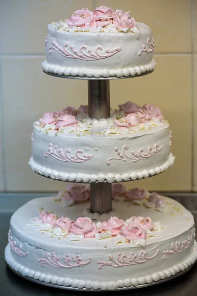 La torta nuziale a tre livelli è decorata con fiori e si trova sul tavolo accanto a un piatto e posate. — Foto Stock