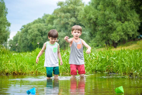 Dos hermanitos jugando con barcos de papel junto a un río en un cálido y soleado día de verano . —  Fotos de Stock