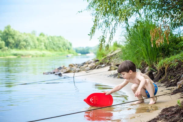 Хлопчик грає з корабельною іграшкою в морі. Дитячі ос у відпустці влітку на пляжі у відпустці — стокове фото