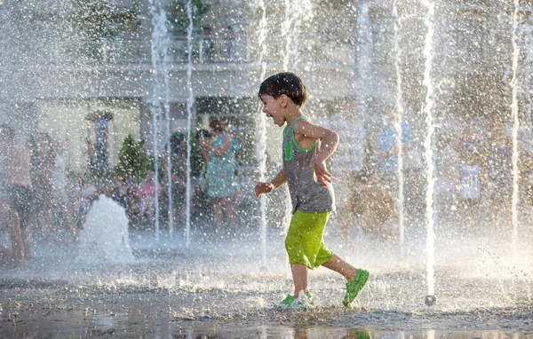 Ragazzo eccitato divertirsi tra getti d'acqua, in fontana. Estate i — Foto Stock