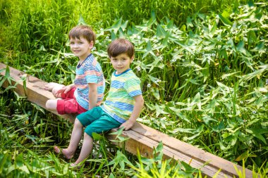 İki sevimli küçük çocuklar bir ahşap köprü üzerinde oturan