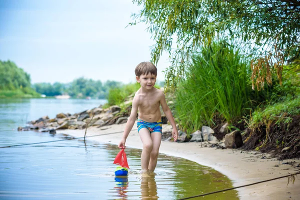 Niño jugando con el juguete del barco en el mar. Niño os de vacaciones en verano en la playa de vacaciones — Foto de Stock