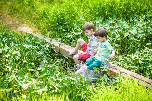 Two cute little boys sitting on a wooden bridge — Stock Photo, Image