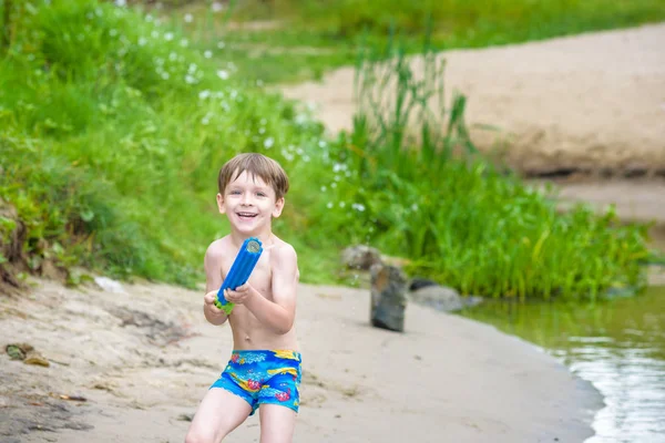 Retrato de niño caucásico en sombrero de paja jugando juguetes y bomba de agua en la playa . — Foto de Stock