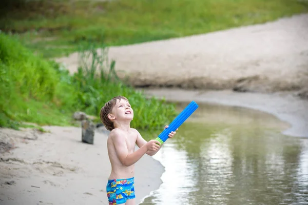 Retrato de niño caucásico en sombrero de paja jugando juguetes y bomba de agua en la playa . — Foto de Stock