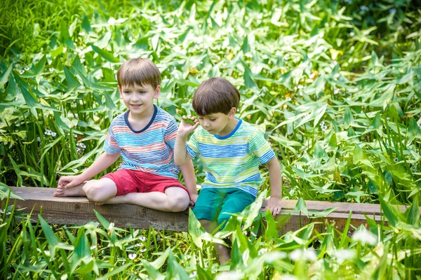 Dos lindos niñitos sentados en un puente de madera — Foto de Stock