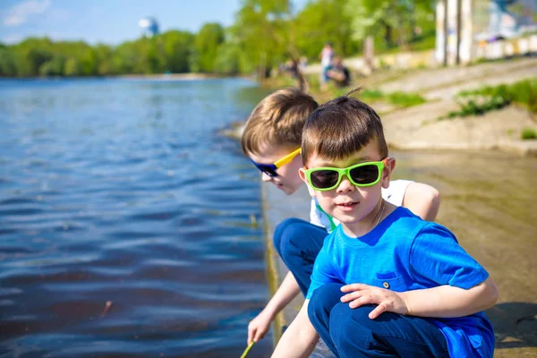 Niños jugando al aire libre en la naturaleza: sentados en el lago o la orilla del río tocando arena en aguas cristalinas en el cálido día de verano o primavera . —  Fotos de Stock