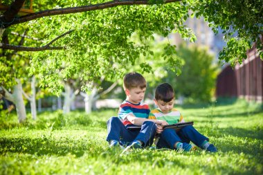 İki kardeş çocuk tablet ile çim üzerinde yalan.
