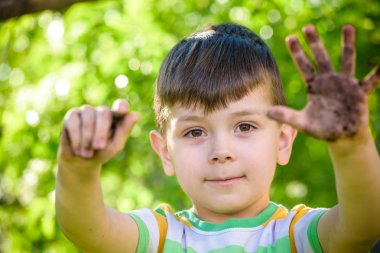 Toprak ve kum oynadıktan sonra kirli ellerini gösterilen genç bir beyaz çocuk