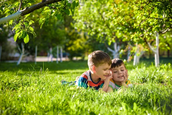 Niños felices divirtiéndose al aire libre. Niños jugando en el parque de verano. Pequeño niño y su hermano acostado en verde campo de vacaciones de hierba fresca . — Foto de Stock