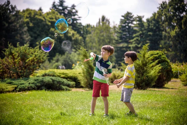 Chico soplando burbujas de jabón mientras un niño emocionado disfruta de las burbujas — Foto de Stock