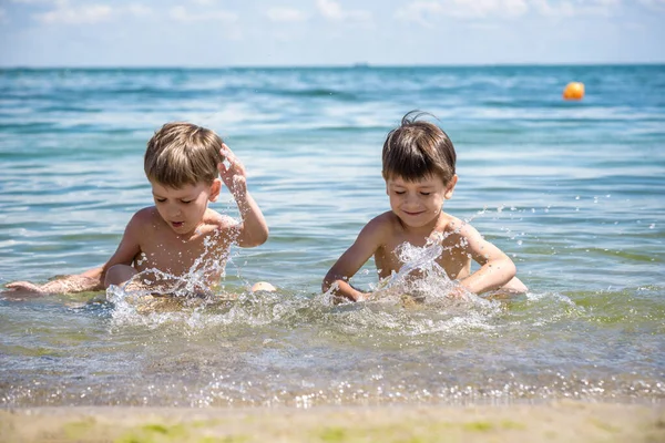 Familia feliz jugando en el agua azul de la piscina en un complejo tropical en el mar. Concepto de vacaciones de verano. Dos hijos hermanos son mejores amigos. — Foto de Stock