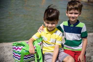 İki güzel kardeş kardeş yelek ve şortlu dalgakıran üzerinde yazın denize ve kıyıya karşı oturuyorlar. Anaokulu çocukları en iyi arkadaşlar deniz kenarında yaz tatilinin tadını çıkarıyorlar.