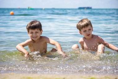 Denizde tropik bir tatil köyünde mavi yüzme havuzunda oynayan mutlu bir aile. Yaz tatili konsepti. İki kardeş çok iyi arkadaştır.