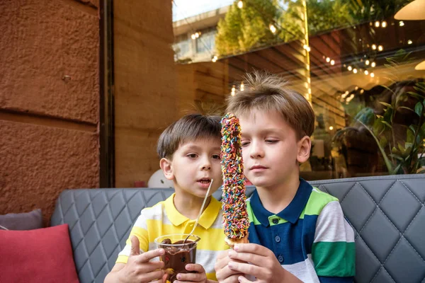 Two young brother boy eating waffle with chocolate and multicolored sugar sprinkles outdoor and fondue fruits. Unhealthy tasty sweet food concept — Stock Photo, Image