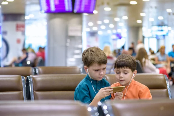 Два мальчика, сидящих в зале вылета из аэропорта, довольны — стоковое фото