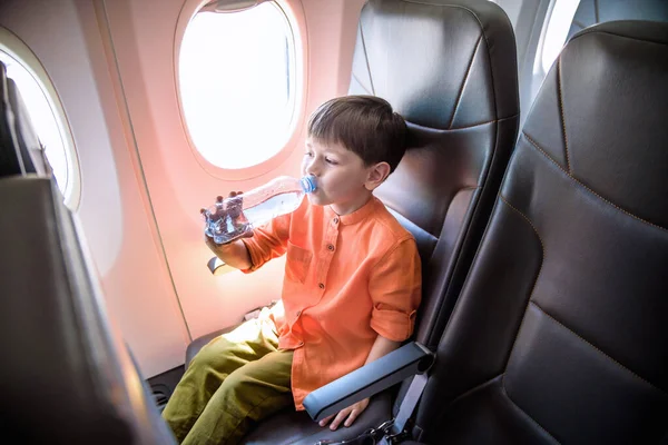 Чарівна дитина подорожує літаком. Маленький хлопчик п'є воду — стокове фото