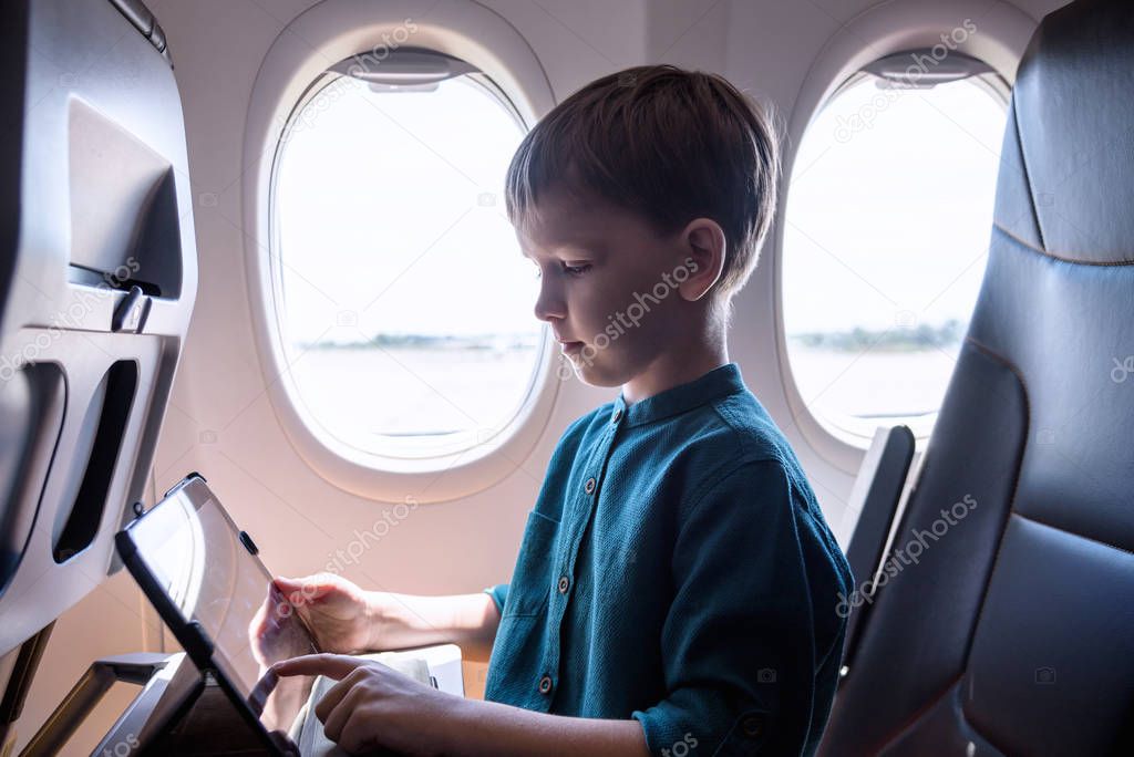 Cute six years old boy, playing on tablen in aircraft on boar, t