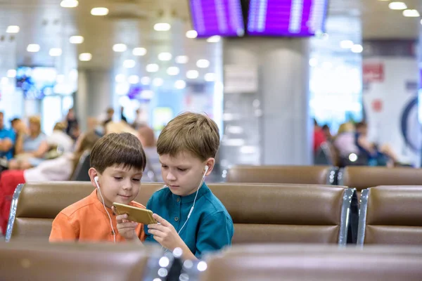 Двоє маленьких хлопчиків сидять у залі вильоту аеропорту за змістом — стокове фото