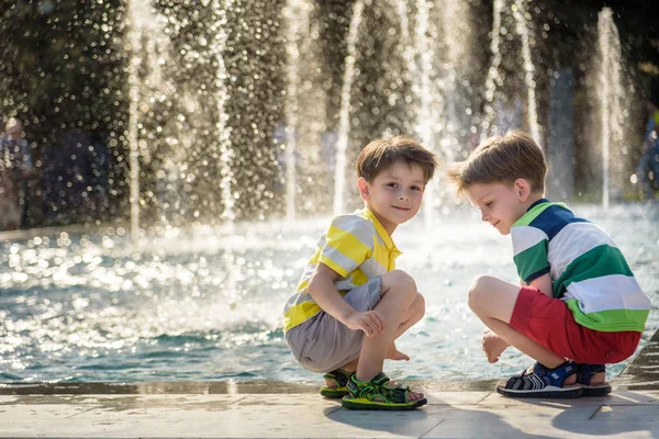 Bébé mignon garçon et frères aînés, jouer sur une fontaine à jet avec éclaboussures d'eau autour, été — Photo