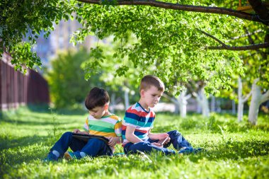 İki kardeş çocuk tablet ile çim üzerinde yalan.