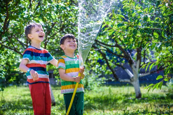 Rapaz feliz derrama água de uma mangueira — Fotografia de Stock