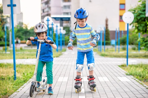 İki tekerlekli paten ve kardeş kardeşi parkta sarılmış scooter üzerinde çocuk evlat. Çocuk koruma vatkaları güvenli paten için binmek. Çocuklar için etkin açık spor.
