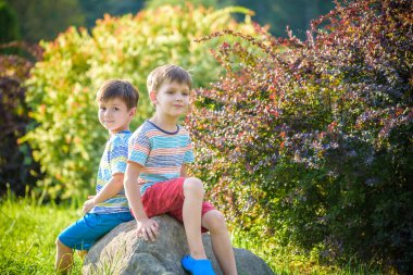Bir kaya üzerinde güneşli parkta oturan iki çocuk akşam veya gün konusunda sizi uyarır. Sezon, çocuklar, yaşam tarzı kavramı.