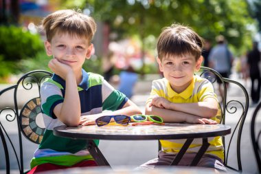 İki küçük çocuk otel restoranında ya da şehir kafesinde sağlıklı bir kahvaltı için masada bekliyor. Çocuk rahat sandalyeye oturur, rahatlar, tatilinin tadını çıkarır. Çocuk konseptiyle yaz tatili.
