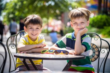 İki küçük çocuk otel restoranında ya da şehir kafesinde sağlıklı bir kahvaltı için masada bekliyor. Çocuk rahat sandalyeye oturur, rahatlar, tatilinin tadını çıkarır. Çocuk konseptiyle yaz tatili.