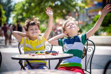 İki küçük çocuk otel restoranında ya da şehir kafesinde sağlıklı bir kahvaltı için masada bekliyor. Çocuk elleri havada rahat bir sandalyeye oturur, rahatlar ve tatilinin tadını çıkarır. Çocuk konseptiyle yaz tatili.