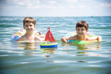 Mutlu çocuklar sahilde sörf yaparken eğleniyor. Şen şakrak bir çift çocuk kırılma dalgasında şişirilebilir ring gezintisinde. Seyahat yaşam tarzı, aile yaz kampında yüzme aktiviteleri. Tropikal adada tatiller.