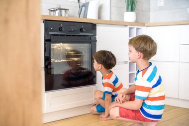 Çocuklar mutfakta oynuyorlar ve fırında bisküvi pişirmeyi bekliyorlar. İki kardeş evde yemek pişiriyor..