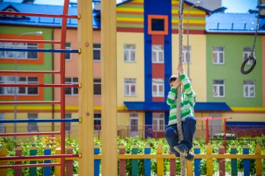 Oyun parkında ip tırmanmaktan hoşlanan şirin bir çocuk. Küçük çocuk tırmanmayı öğreniyor, güneşli bahar gününde eğleniyor. Çocuklarla aktif eğlence.