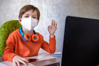 Coronavirus salgını. Kilitlenme ve okul kapanması. Yüz maskeli okul çocuğu evde sıkılmış ve depresif hissederek online eğitim dersleri izliyor. COVID-19 salgını çocukları çevrimiçi öğrenmeye zorluyor.