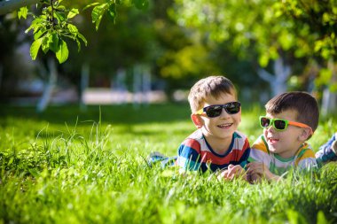 Mutlu gülümseyen erkek kardeş kardeşi çimenlerin üzerinde rahatlatıcı. Kopya alanı görünümüyle kapatın. Okul öncesi çocuklar güneş gözlüğü takıyor yaz tatil kampı. Gevşeme mutlu çocukluk dostluk kavramı.