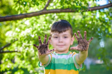 Çamur ve kumsalda oynadıktan sonra kirli ellerini gösteren beyaz bir çocuk. Güneşli bahar ya da yaz akşamları çiçek ağaçlarının arka planında. Mutlu çocukluk arkadaşlığı kavramı.