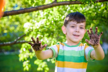 Çamur ve kumsalda oynadıktan sonra kirli ellerini gösteren beyaz bir çocuk. Güneşli bahar ya da yaz akşamları çiçek ağaçlarının arka planında. Mutlu çocukluk arkadaşlığı kavramı.
