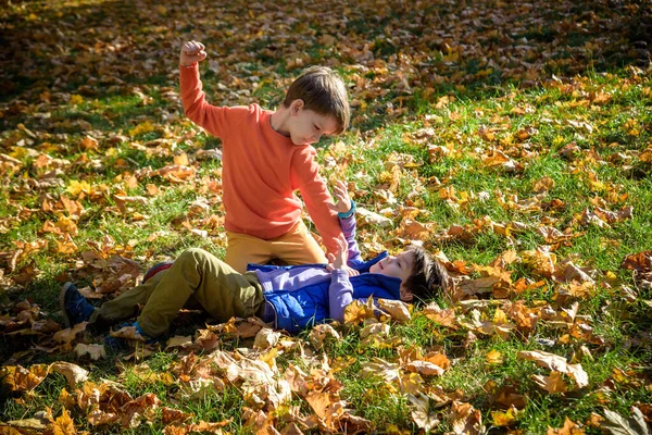 Two boys fighting outdoors. Friends wrestling in summer park. Siblings rivalry. Aggressive kid hold younger boy on ground, try to hit him.