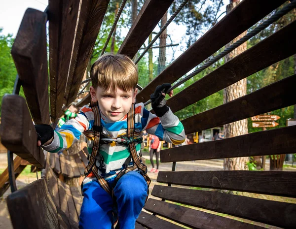 Happy kid overcomes obstacles in rope adventure park. Summer holidays concept. Little boy playing at rope adventure park. Modern amusement park for kids. Outdoors games