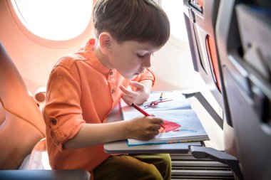 Uçakla seyahat eden sevimli bir çocuk. Neşeli küçük çocuk uçuş sırasında uçak penceresinin yanında oturuyor. Küçük çocuklarla hava yolculuğu..