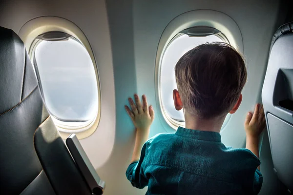 A boy have flight looking in the airplane window or porthole.