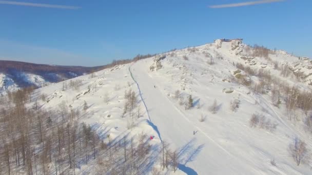 Sciatori e snowboarder scivolano lungo la montagna vicino al lago di Bannoe. Aerea — Video Stock