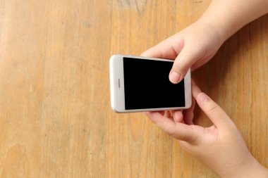 Üst düzey kadın elinde tutuyor ve ahşap masa üzerinde akıllı telefon kullanıyor.