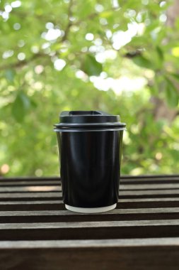 Yeşil yapraklı ahşap üzerine siyah kağıt kahve fincanı.